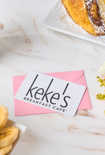 Keke's Breakfast Cafe gift card in a pink envelope surrounded by coffee, Nutella-stuffed French toast, fresh fruit, and flowers