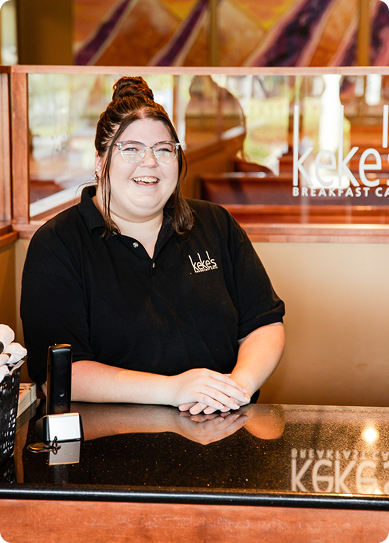 Smiling Keke's Breakfast Cafe team member at the host stand wearing a branded polo