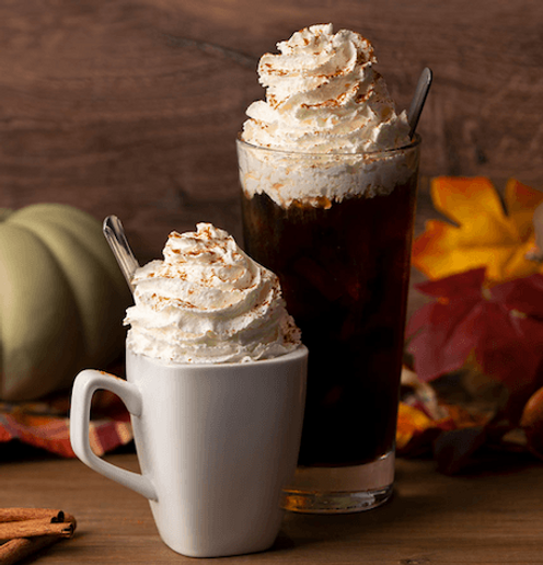 Pumpkin pie coffee topped with whipped cream and cinnamon in a clear mug, with mini pumpkins in the background