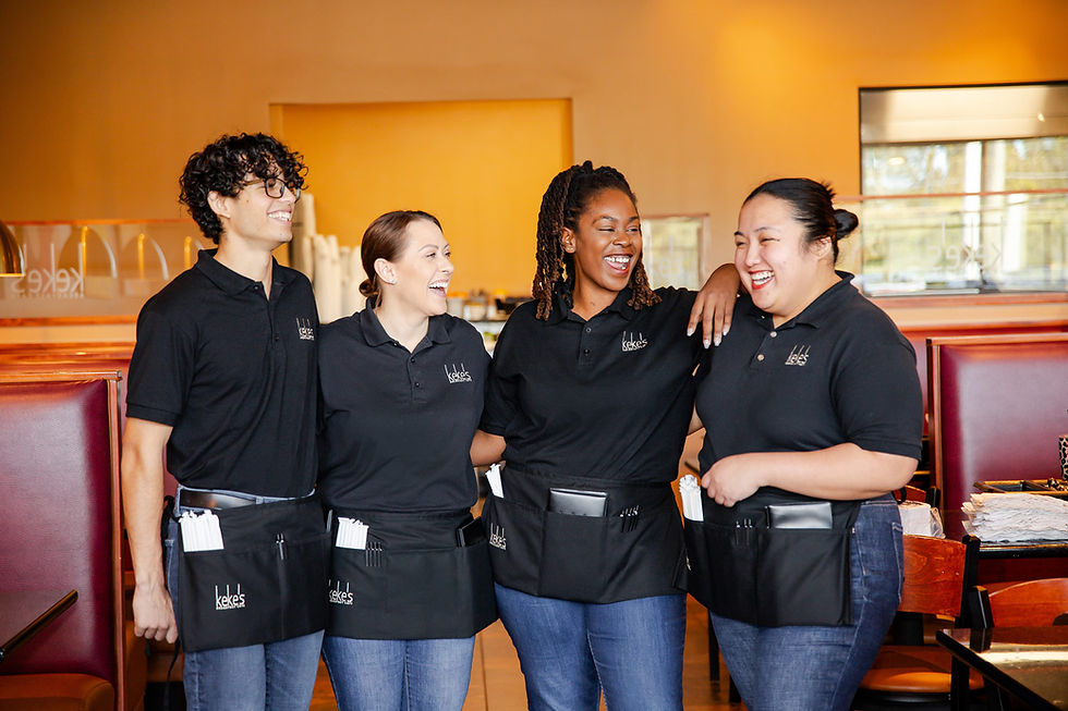 Four Keke's Breakfast Cafe team members in branded uniforms standing together in the dining area